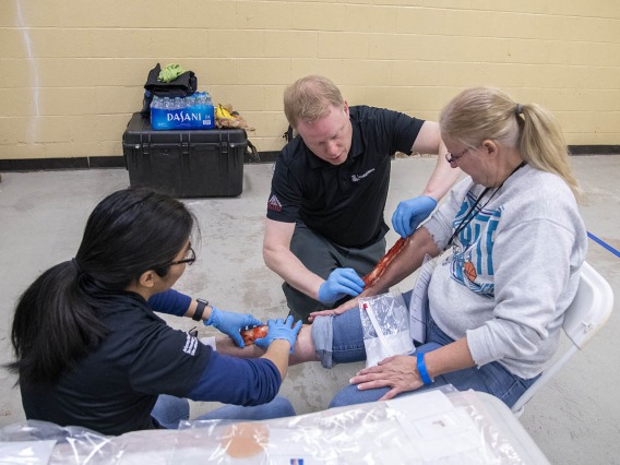Merryl Lopido, simulation operations specialist for ASTEC, and David Biffar, ASTEC’s assistant director of operations, use special-effects makeup to simulate traumatic injuries on volunteer Helen Ward’s leg. Many volunteers received simulated wounds with fake blood or embedded debris.