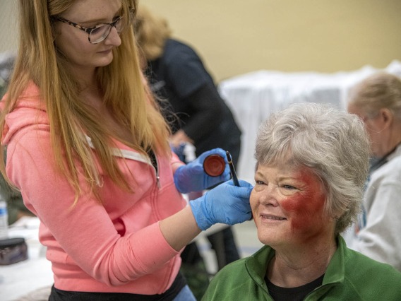 Sadie Keesler, an undergraduate at the University of Arizona College of Science and ASTEC volunteer, creates a burn effect on volunteer Deborah Tilley. Tilley said she was excited to Skype her grandchildren and show them her simulated wounds.