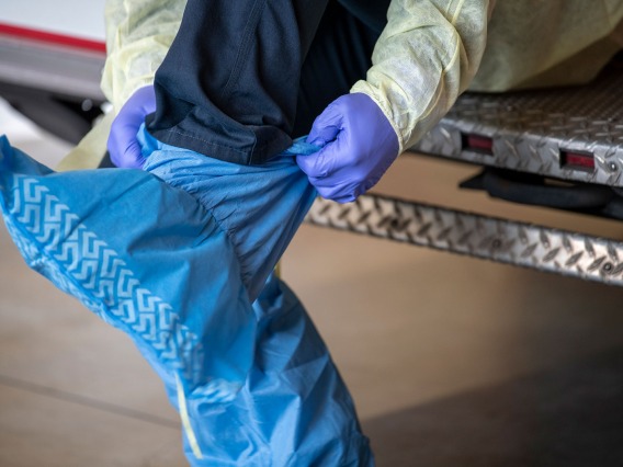 Tucson Fire Department’s Taylor Parrish puts on a protective gown and boot coverings to prevent spread of disease before entering the home a possible COVID-19 patient.