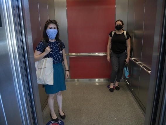 First-year College of Medicine – Tucson students Aileen Lee (left), and Brianne Davis (right) stand on signs placed on elevator floors marking six feet.