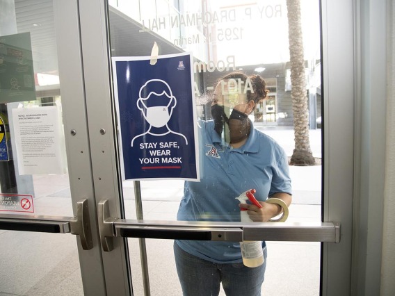 Alexandra Almli from University of Arizona Facilities Management cleans a door at the Mel and Enid Zuckerman College of Public Health before placing new signage.