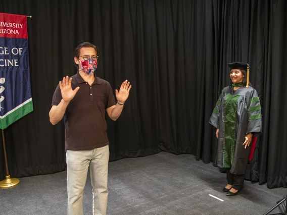 Gilberto Vega shows medical student Cazandra Zaragoza how to simulate walking across a stage on graduation day. College of Medicine – Tucson student photos and videos will be used in the college’s virtual convocation event.