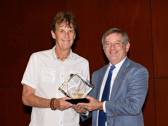 Older man wearing a white short-sleeved button-up shirt (Dr. Nicholas Delamere) receives an award from a man wearing a gray suit representing the Association for Research in Vision and Ophthalmology.