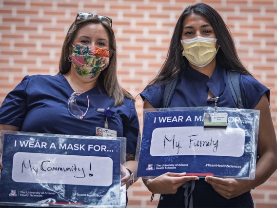 Maria Williams and Elizabeth Mata, third-year College of Medicine – Tucson students, share their signs. Williams wears a mask for her community and Mata wears a mask for her family. 