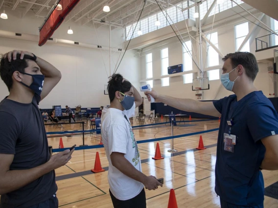 University of Arizona student Heath Zuniga (left) watches as Wyatt Snell, a clinical research coordinator, takes student Mason Young’s temperature prior to the self-administered COVID-19 testing procedure.