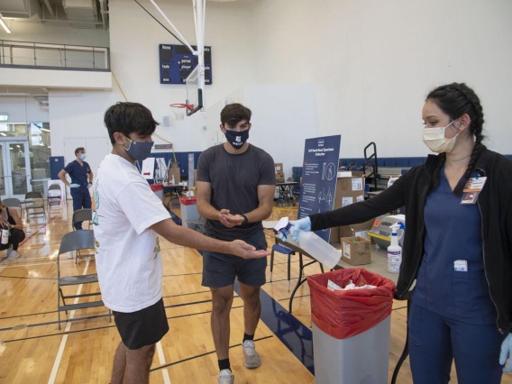 Clinical research coordinator Brenna Abril provides sanitizer spray for students Mason Young and Heath Zuniga after they take an antigen test at the University of Arizona Recreation and Wellness Center, known as NorthREC, in Tucson.