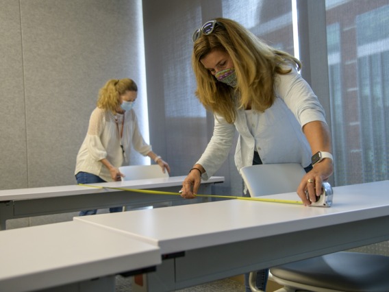 Mary Matthews, left, and Angie Souza, right, of Health Sciences Planning and Facilities, measure the distance between desks in the Health Sciences Innovation Building to design new seating arrangements to ensure people stay six feet apart.
