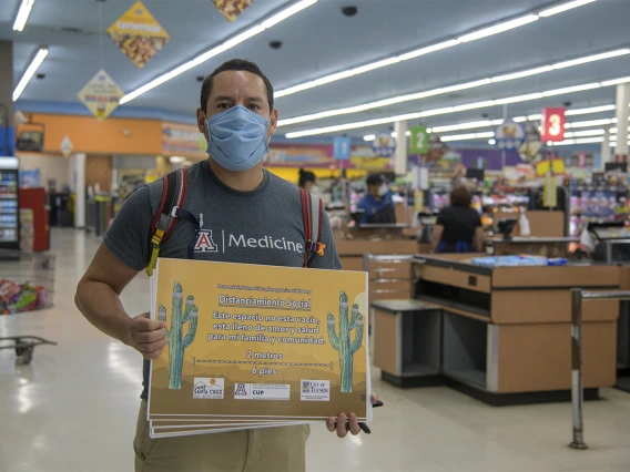 Fourth-year medical student Ricardo Reyes co-led a student-run effort to create Spanish-language social distancing signage. Reyes hangs a sign in a Food City grocery store on South Sixth Avenue in Tucson in May.