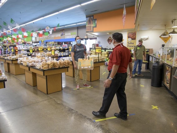 Fourth-year medical student Ricardo Reyes joins Food City Store Manager Ramon Lopez show what social distancing looks like at the store on West Ajo Way by staying six feet apart, using the lines on the floor of the grocery store as guides.
