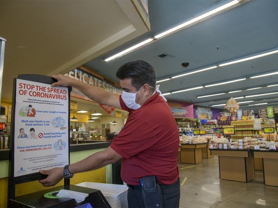 Store Manager Ramon Lopez hangs a “stop the spread poster” from the Pima County Health Department at the Food City grocery store on West Ajo Way.