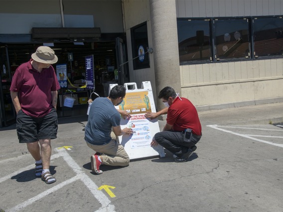 A customer walks by as fourth-year medical student Ricardo Reyes and Ramon Lopez, store manager of the Food City on West Ajo Way in Tucson, hang a social distancing poster at the entrance of the store. Reyes and his peers in the College of Medicine – Tucson designed many of the posters as outreach about ways to practice health precautions for Spanish-speaking communities in Arizona.