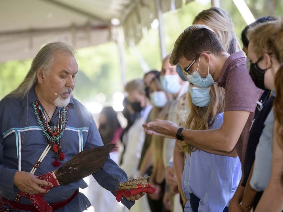 During the smudging ceremony, Dr. Carlos Gonzales holds the shell containing the burning herbs for a student to pull the smoke over himself as part of the blessing. 