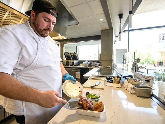 A male chef with a white coat puts food onto a tray on a counter.