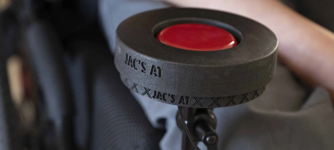 Close-up of a large red button in a black plastic holder secured to a wheelchair