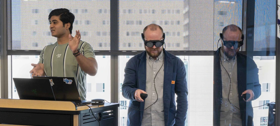 professor wearing VR goggles reviews a student’s VR project