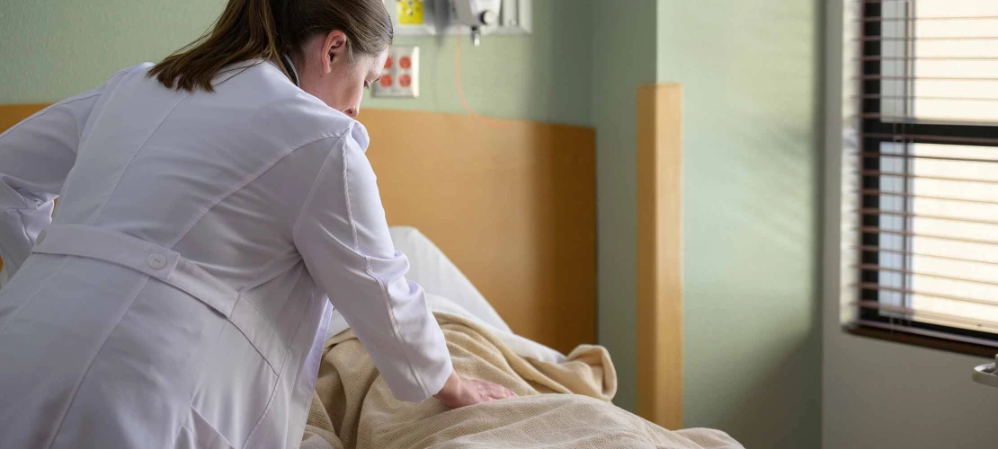 doctor wearing white coat standing at patient bedside with hand on patient stomach