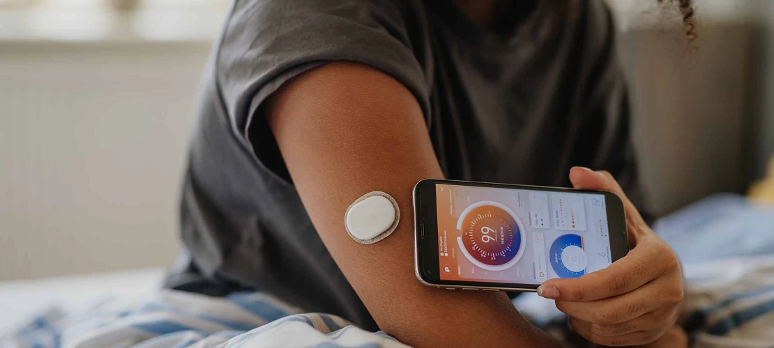 close-up of person's arm with glucose monitor on the skin and holding a cell phone to read the monitor