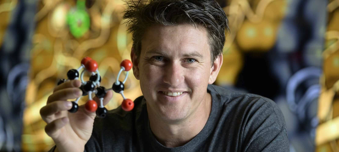 A person holding a detailed model of a molecule represented by spheres connected by curved bars
