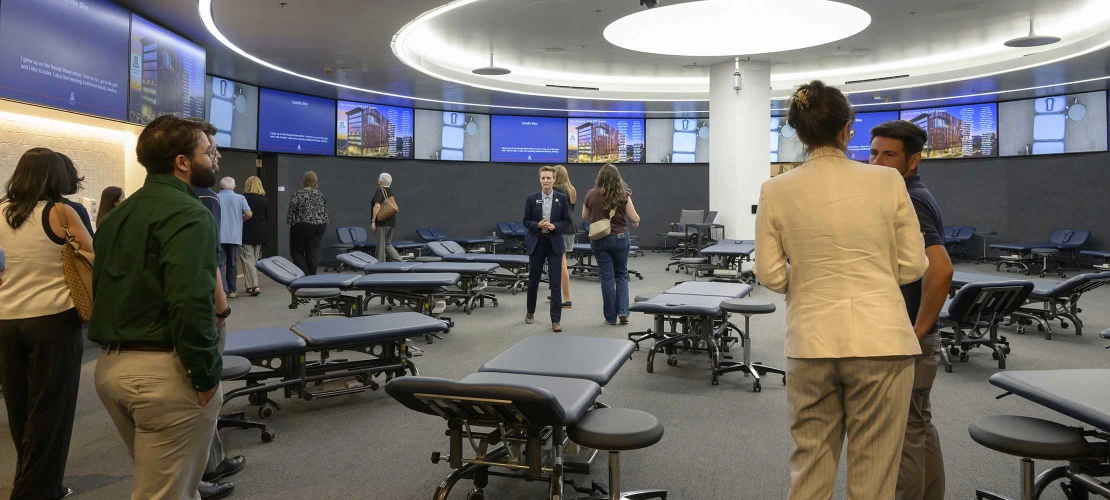 Photo of several people chatting together in a circular room filled with examining tables in the new lab space of the University of Arizona School of Health Professions Physical Therapy and Physician Assistant studios.