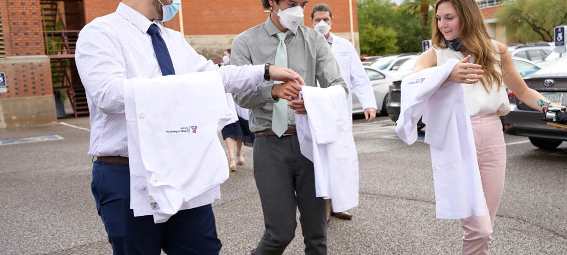 Members of the UArizona College of Medicine – Tucson Class of 2026 discuss how to properly fold their coats as they walk to the ceremony at Centennial Hall.
