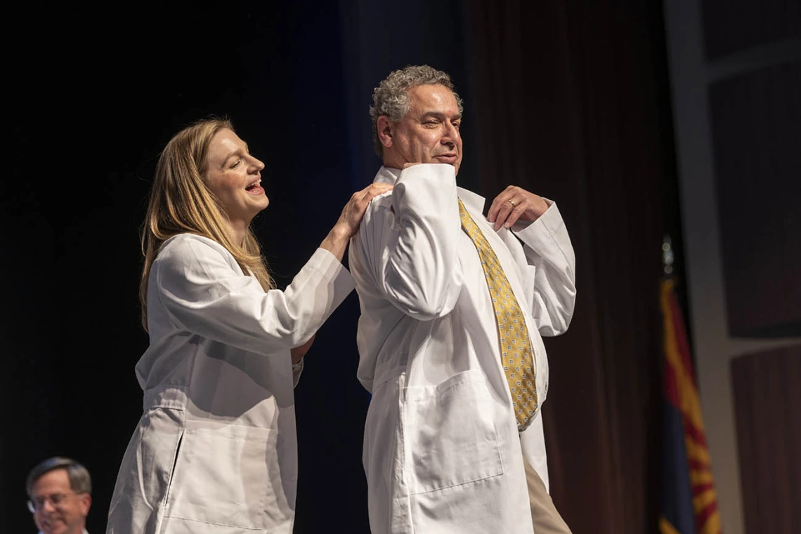 Professor Lindsay Bouchard helps Michael Nango with his white coat at the UArizona College of Nursing white coat ceremony.