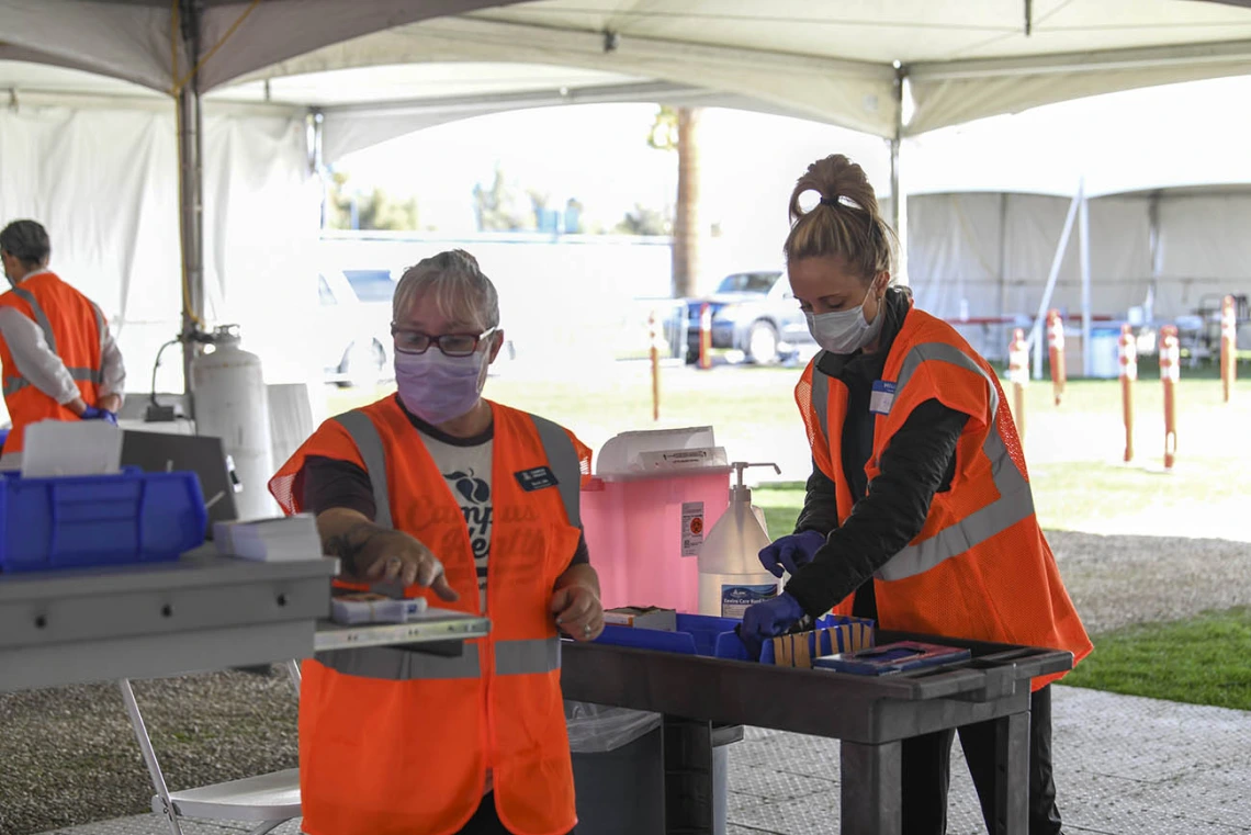 Volunteer Becky Dillie, left, prepares to log information in her computer as volunteer Kerry Johnson sets up to provide vaccinations to drivers with appointments. 