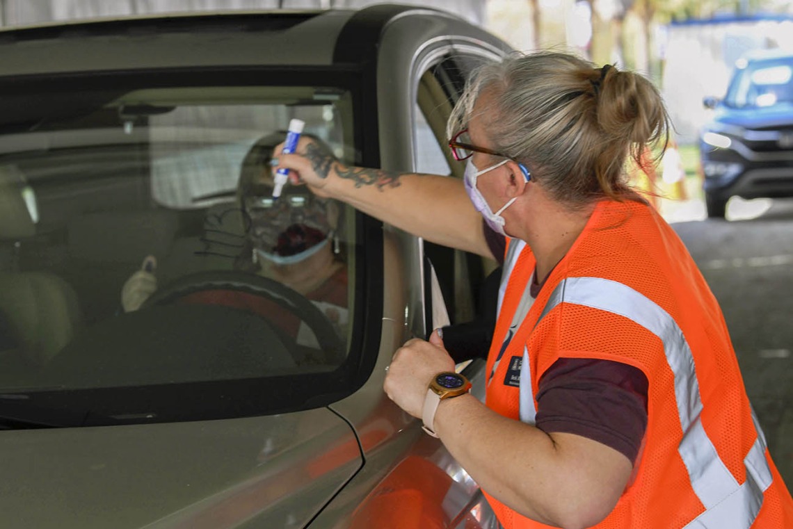 After receiving a vaccine, each driver must wait 15 minutes in their car to ensure no immediate side effects. At the University of Arizona vaccine distribution site, a volunteer writes the vaccination time on a driver’s window.