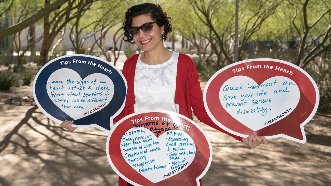 Female professor with dark curly hair wearing sunglasses holds three heart-shaped posters. 