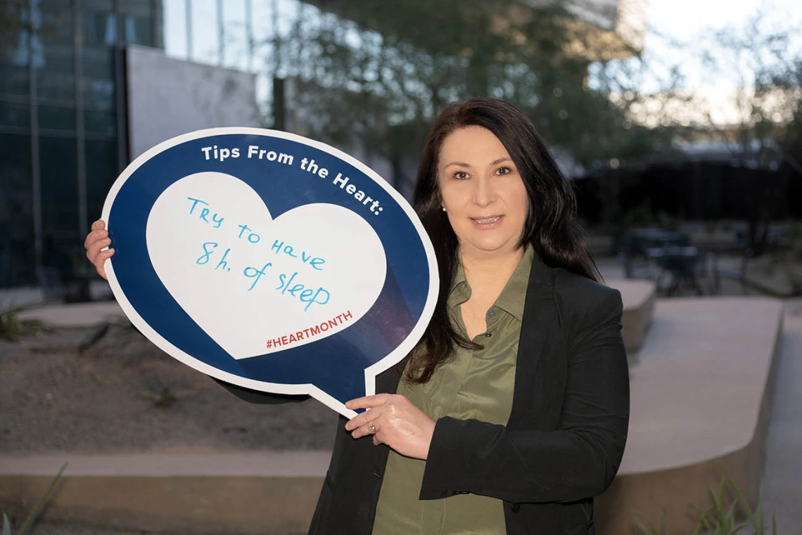 Woman with shoulder-length dark hair holds up sign saying "Try to have 8 hours of sleep"