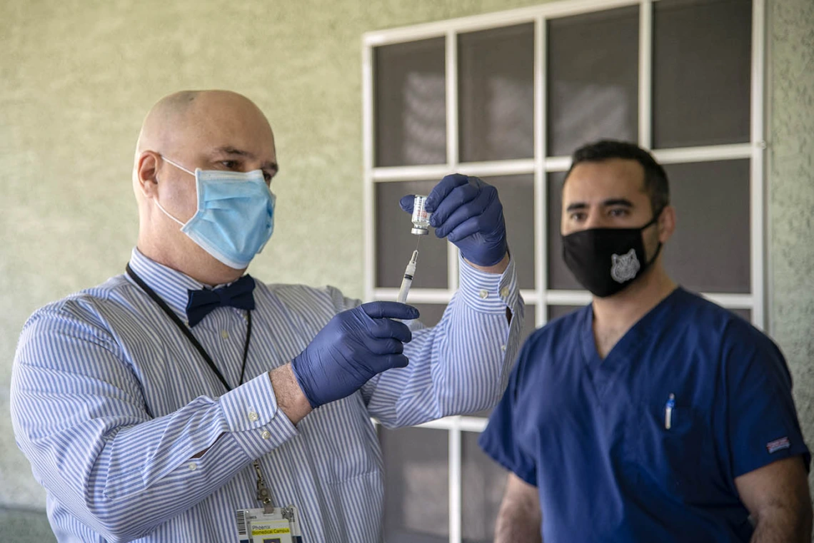 Jim Lindgren, MD, director of simulation curriculum and clinical assistant professor at College of Medicine – Phoenix, prepares a vaccine as Jeffery Hanna, clinical research coordinator, observes.