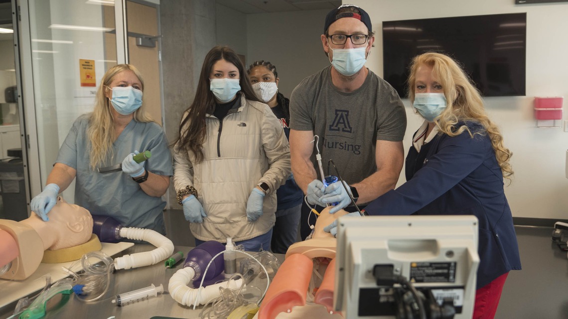 (From left) First year CRNA students Jennifer Heiden, Cameron Wylie and Sabrena Wells (back) observe as Phillip Witte practices performing a GlideScope intubation alongside Kristie Hoch, DNP, CRNA, MS, RRT, at the Arizona Simulation Technology and Education Center. Dr. Hoch is the program administrator for the nurse anesthesia program at the College of Nursing. 