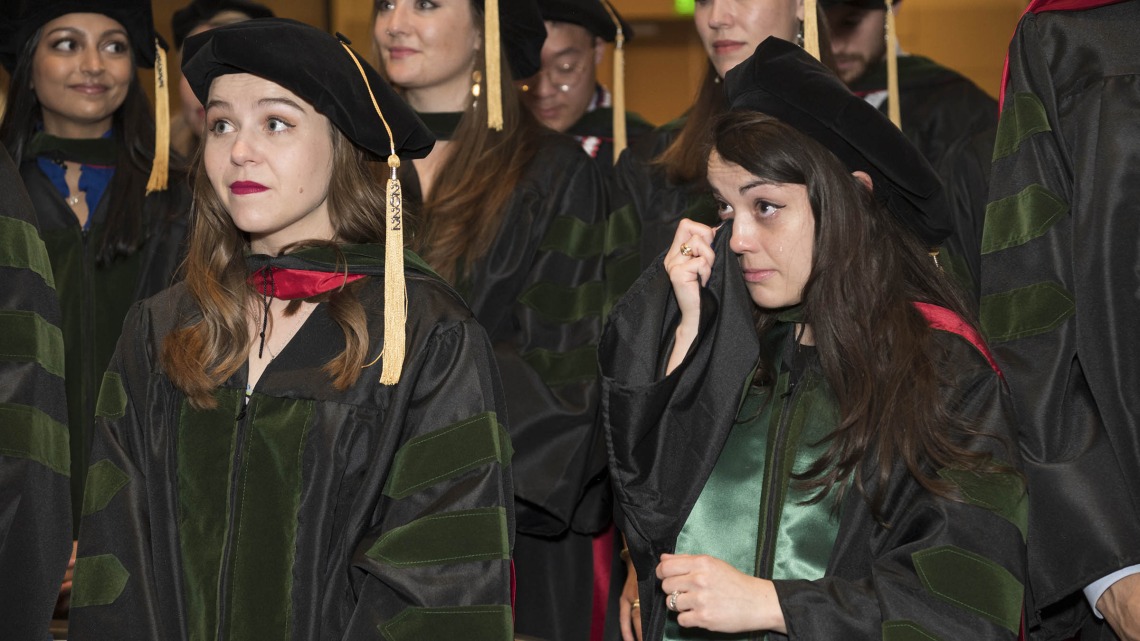 Nicole Deatherage, MD, (front right) wipes a tear from her eye with her graduation gown as she and Merrion Dawson, MD, (left front) listen to speakers during the College of Medicine – Phoenix class of 2022 commencement ceremony.  