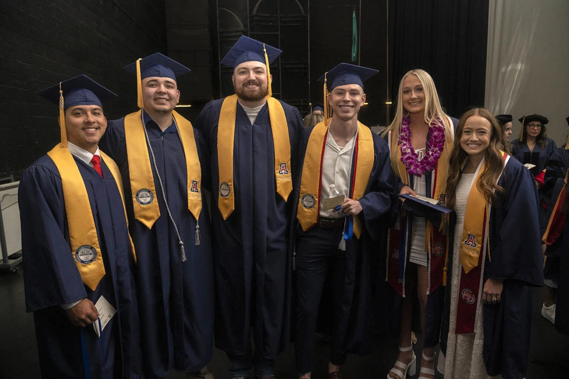 Six people (four male and two female) smile together backstage in Centennial Hall before convocation.