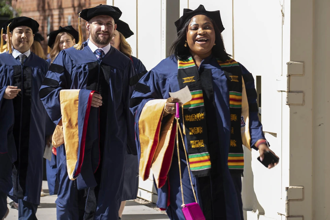 Two men and one woman dressed in graduation cap and gowns proceed into Centennial Hall for convocation.