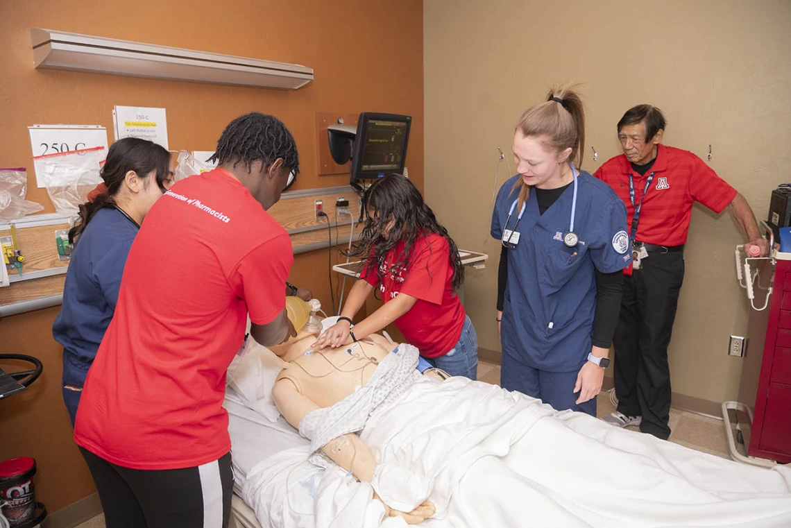 Two kids in practice CPR on a manikin in a clinical setting while nursing students and a professor observe.