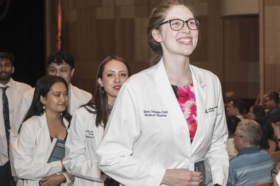 A very happy Emrie Tomaiko-Clark walks out of Symphony Hall in a procession after the UArizona College of Medicine – Phoenix Class of 2026 white coat ceremony in downtown Phoenix.