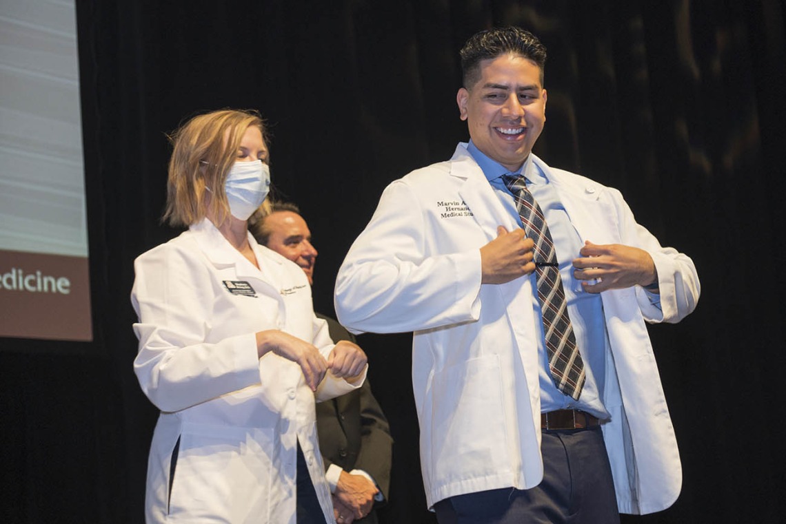 Marvin Alfredo Hernandez receives his white coat from UArizona College of Medicine – Phoenix Associate Dean of Student Affairs Stephanie Briney, DO, during the Class of 2026 white coat ceremony.