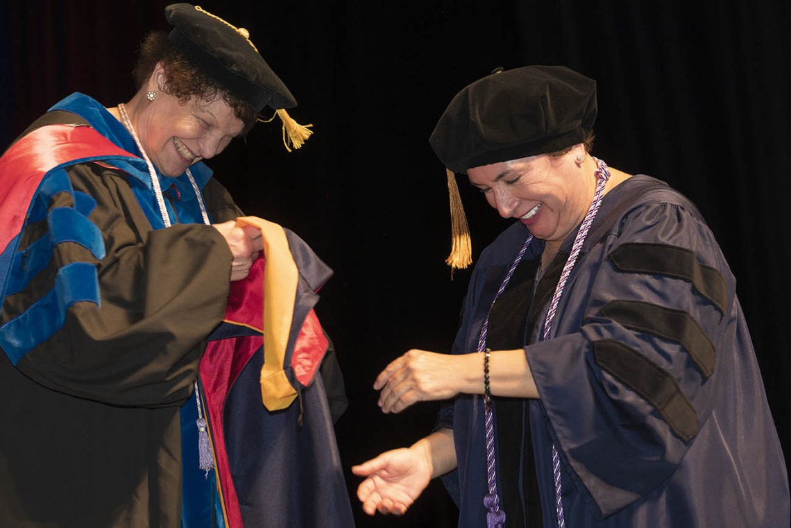 Nicolette Ann Estrada, PhD, MAOM, FNP, (left) an assistant clinical professor in the College of Nursing, prepares to hood Ana Marie Rivera, who earned a Doctor of Nursing Practice degree.