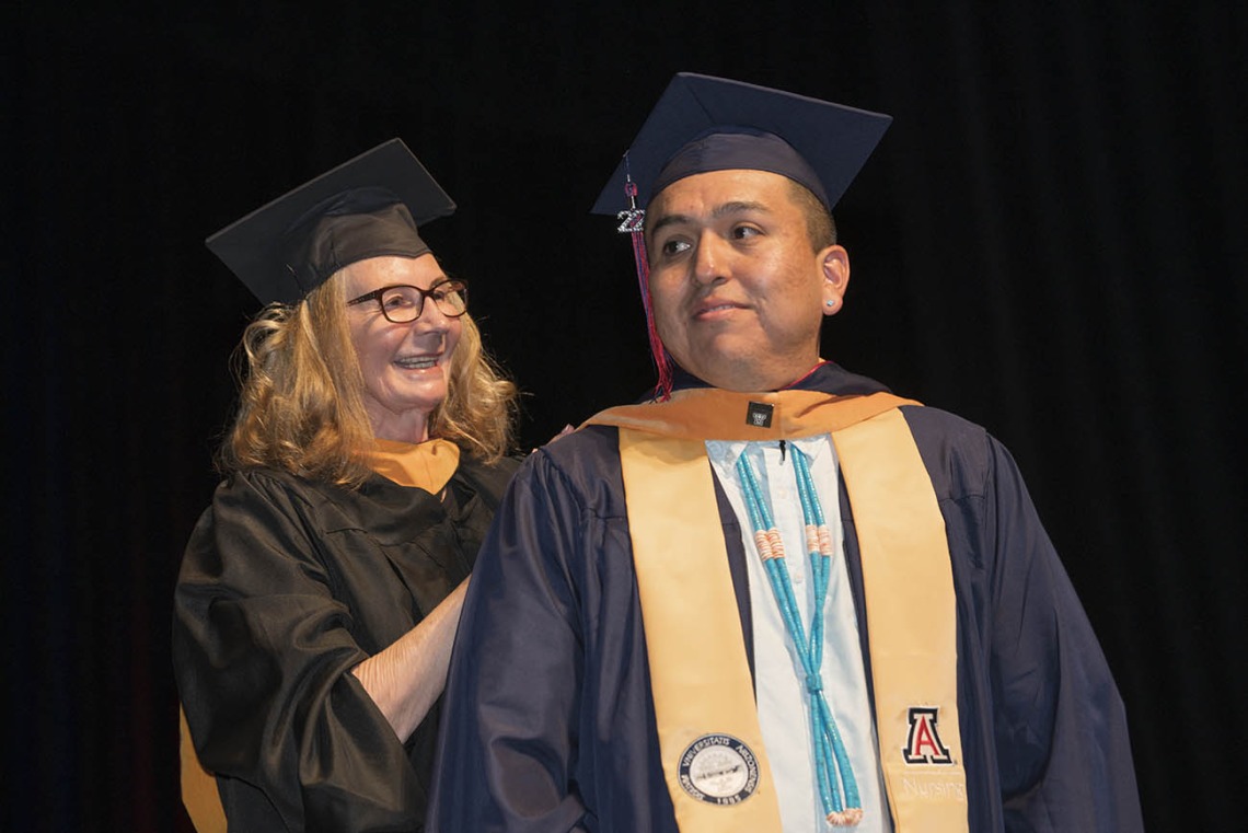 College of Nursing principal lecturer Karen Butterbaugh, MSN, hoods Ryan Whitehorse, who earned a master’s degree in nursing entry to the profession.