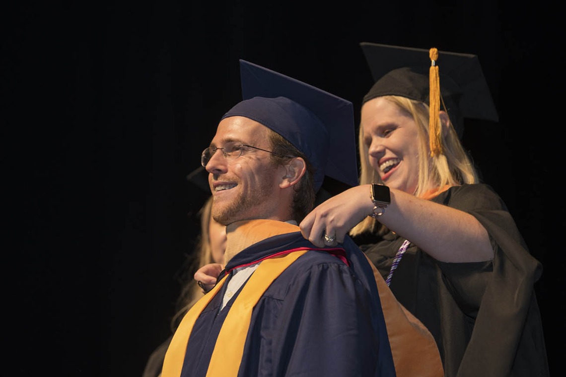 Master of Science in Nursing Entry to the Profession student Marshall Willy-Gravley is hooded by senior lecturer Heidi Kosanke, MSN/Ed, CCRN, during the College of Nursing’s 2022 summer convocation.