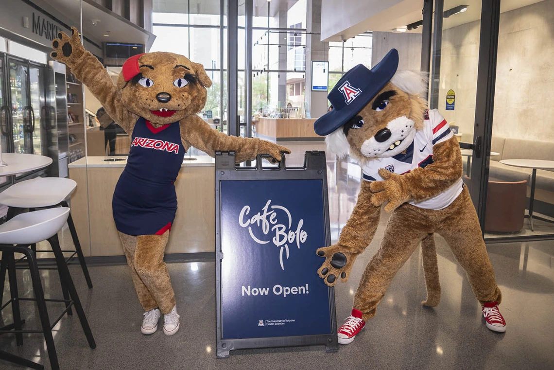 Wilma and Wilbur Wildcat maskcots standing next to a Cafe Bolo sign. 