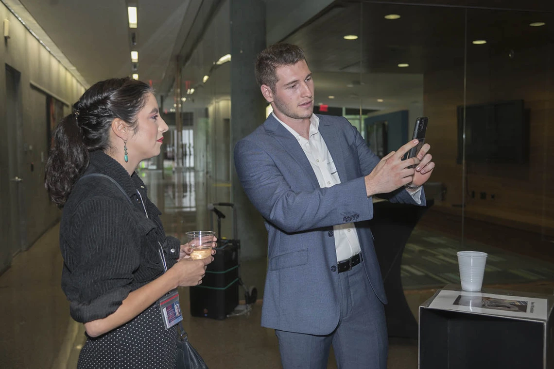 (From left) Nicole Jimenez watches as Zackary Sabetta, a neurotrauma research technician in the College of Medicine – Phoenix, shows the augmented reality artwork created by artist Rembrandt Quiballo titled “It’s All in Your Head—Deconstructing the Brain Concussion” during the public opening of Artist + Researcher exhibition.