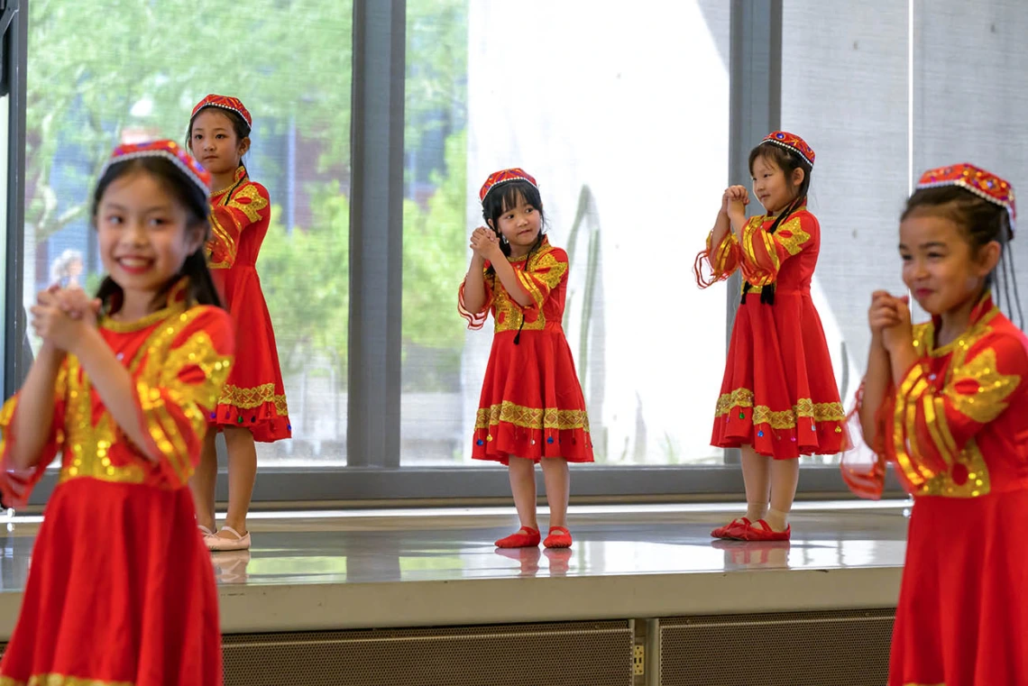 Several young girls from the Tucson Chinese Dance group wear colorful red and gold dresses while performing a dance.