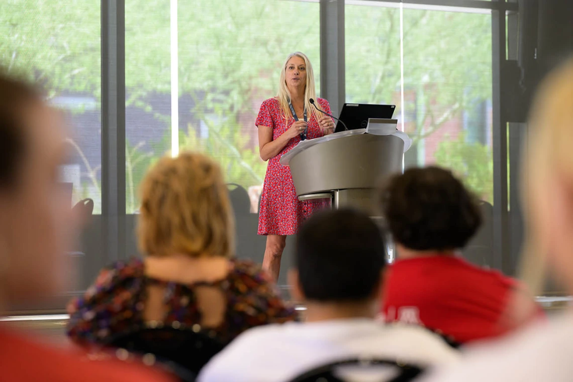 Kelly Reynolds, PhD, stands at a podium speaking to a croud. 