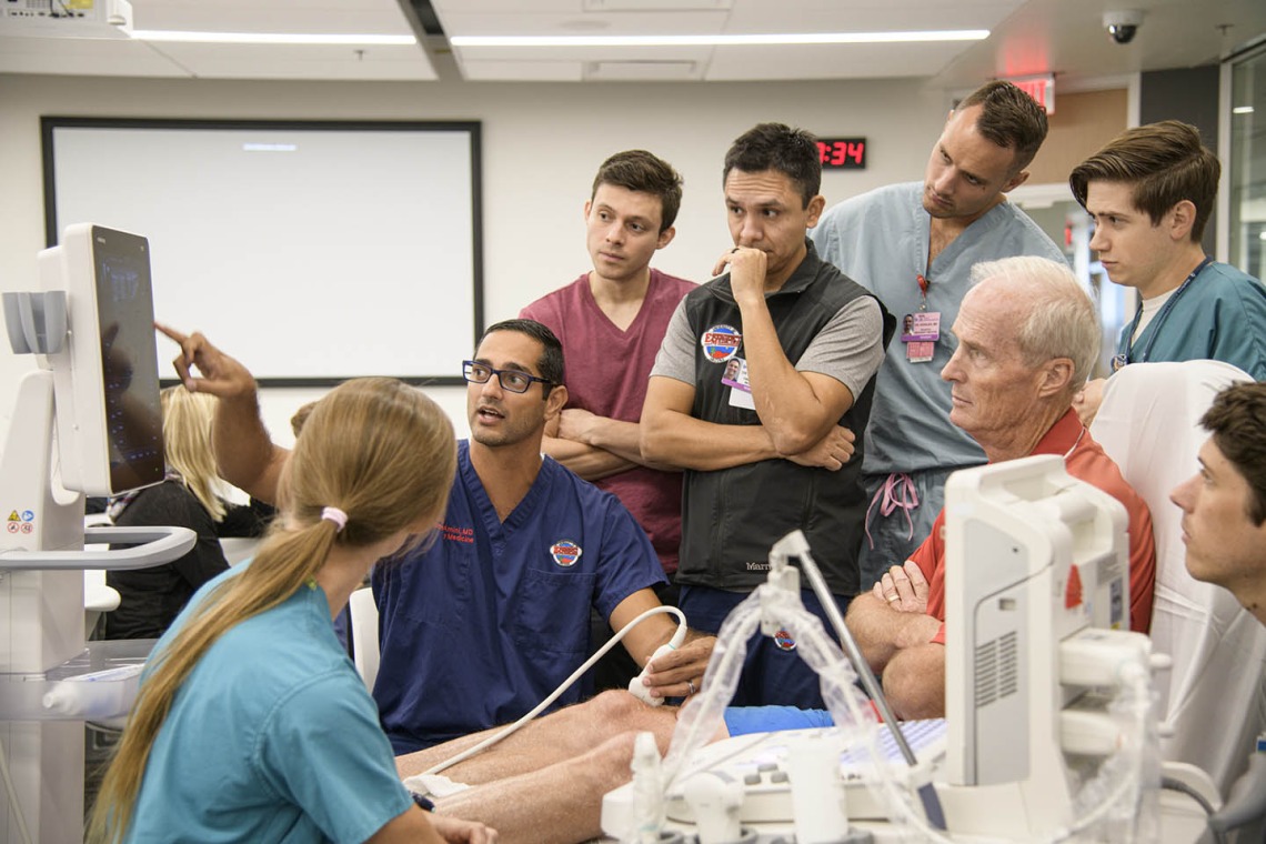 Emergency medicine residents gather around a standardized patient to learn how to administer ultrasound for different injuries.