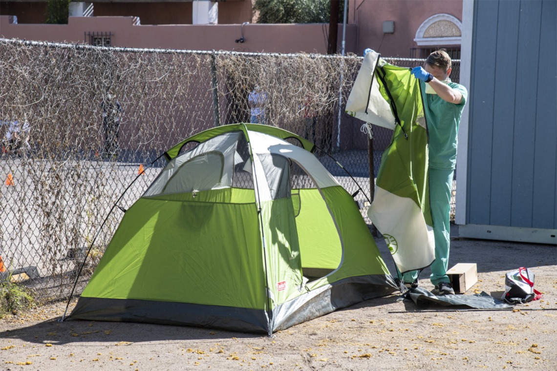 Chris Vance helps set up a tent at the Z Mansion in downtown Tucson. Homeless individuals with potential or suspected coronavirus infection are isolated outdoors in tents on the property. These makeshift “wards” are staffed by UArizona medical students, who distribute food three times a day and monitor patients for worsening conditions.  