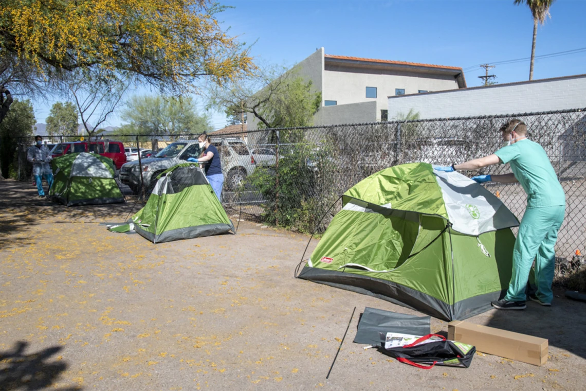 Medical students Christian Bergman (left), Erika Krall, Chris Vance help set up tents at the Z Mansion in downtown Tucson. Homeless individuals with potential or suspected coronavirus infection are isolated outdoors in tents on the property. These makeshift “wards” are staffed by UArizona medical students, who distribute food three times a day and monitor patients for worsening conditions.  