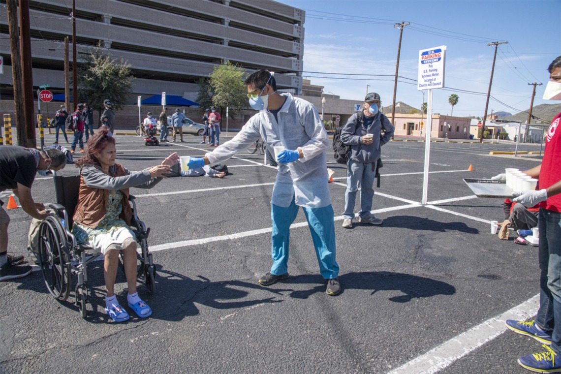Christian Bergman and Shrey Goel offer a drink to a person in the parking lot of the Z Mansion, a soup kitchen for Tucson’s homeless population.