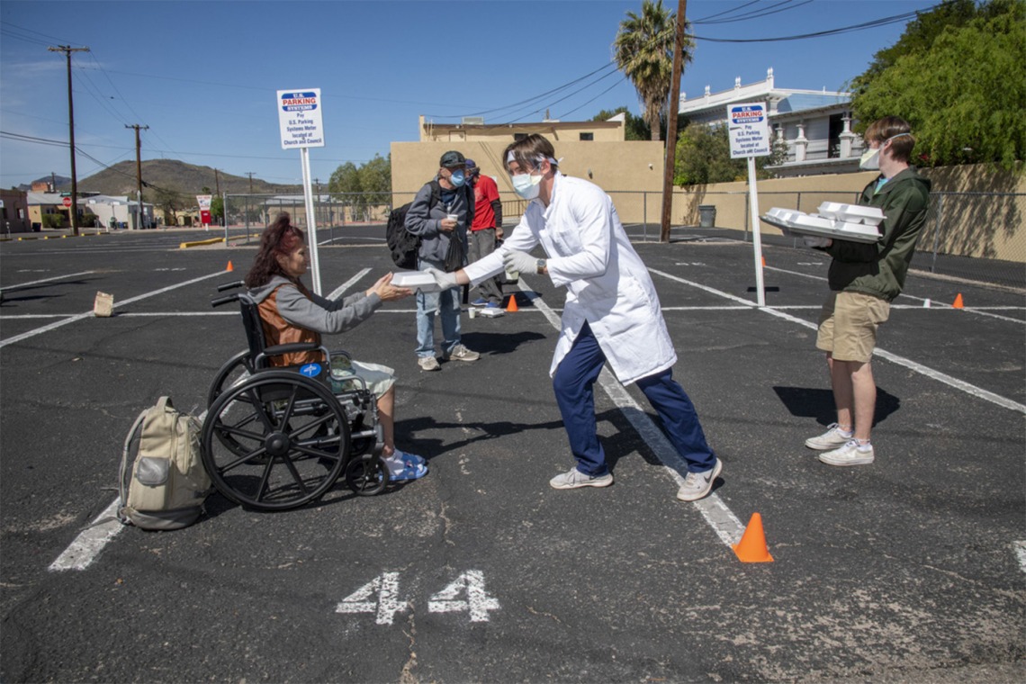 A student in the College of Medicine – Tucson offers food and drink to a woman at Z Mansion, a soup kitchen for homeless people several times a week. They try to keep a safe distance to prevent potential spread of COVID-19 virus.