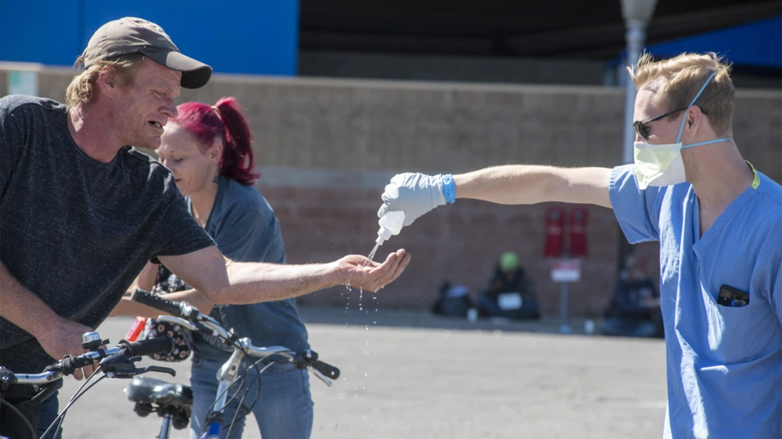 A student in the College of Medicine – Tucson helps a man sanitize his hands. Students are helping homeless people during the pandemic, because the medically-vulnerable population is expected to be hit hard by the COVID-19 virus.